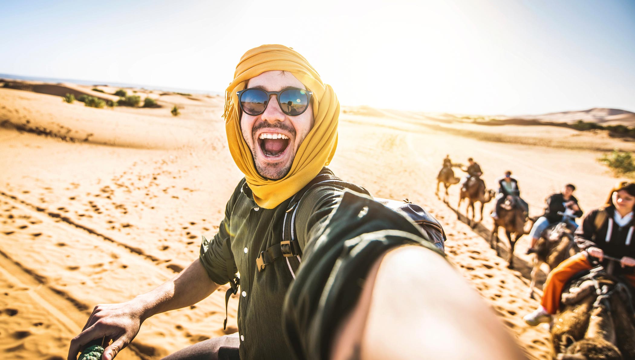 viajes-a-marruecos---viajaldesierto---desierto-de-marruecos--turista-feliz-divirtiéndose-disfrutando-de-un-paseo-en-camello-en-grupo-2023-01-07-03-03-21-utc