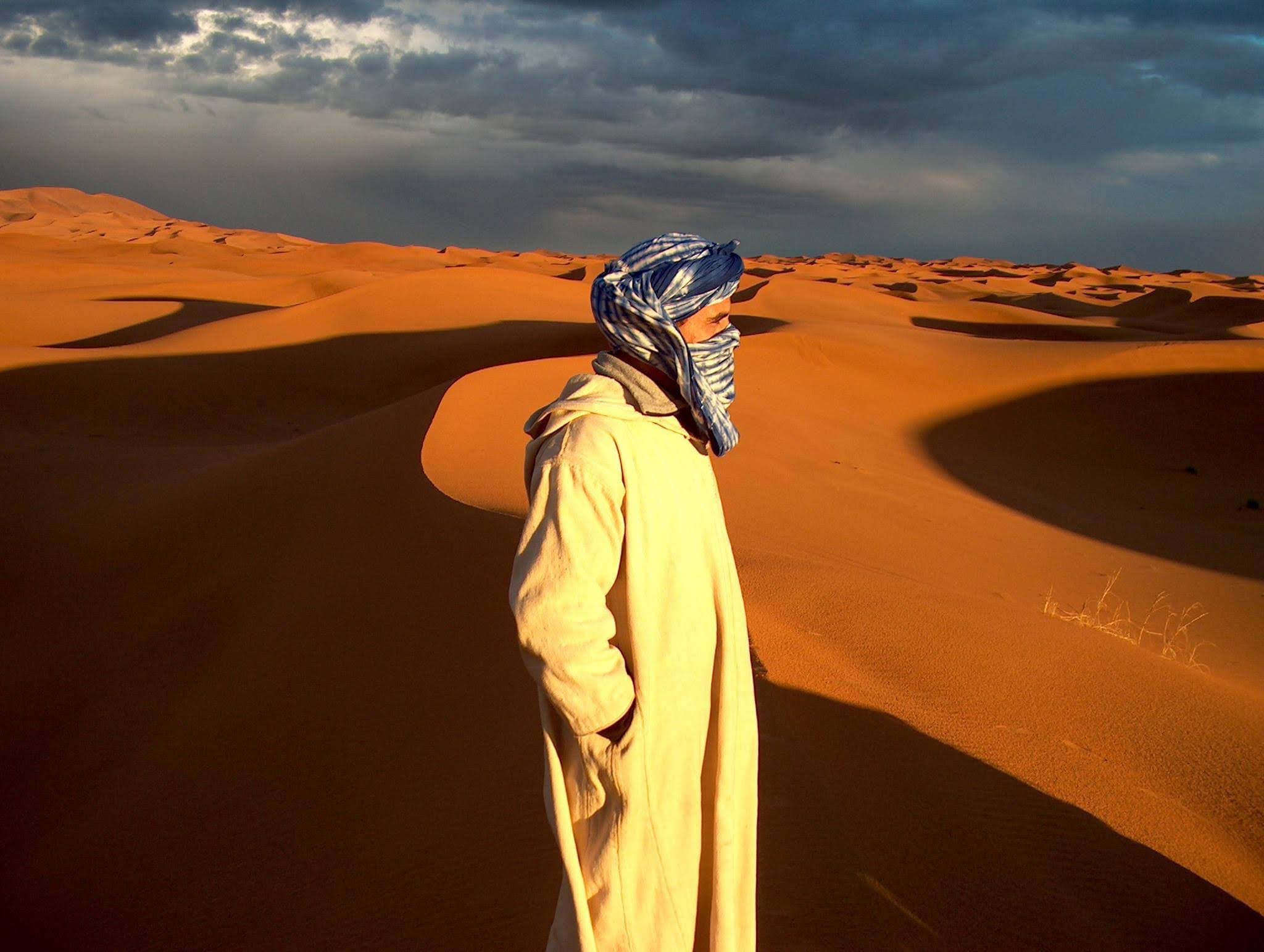 viajes-a-marruecos---viajaldesierto---desierto-de-marruecos--turista-feliz-divirtiéndose-disfrutando-de-un-paseo-en-camello-en-grupo-2023-01-07-03-03-21-utc